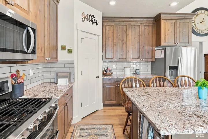Kitchen featuring wood cabinetry, stainless steel appliances, white subway tile backsplash, and light-colored countertops