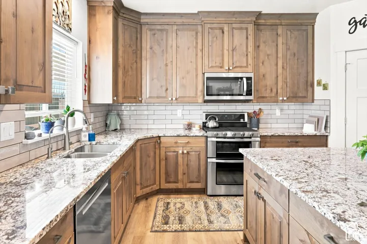 Kitchen featuring wood cabinetry, stainless steel appliances, a double basin sink, light-toned countertops, and a subway tile backsplash