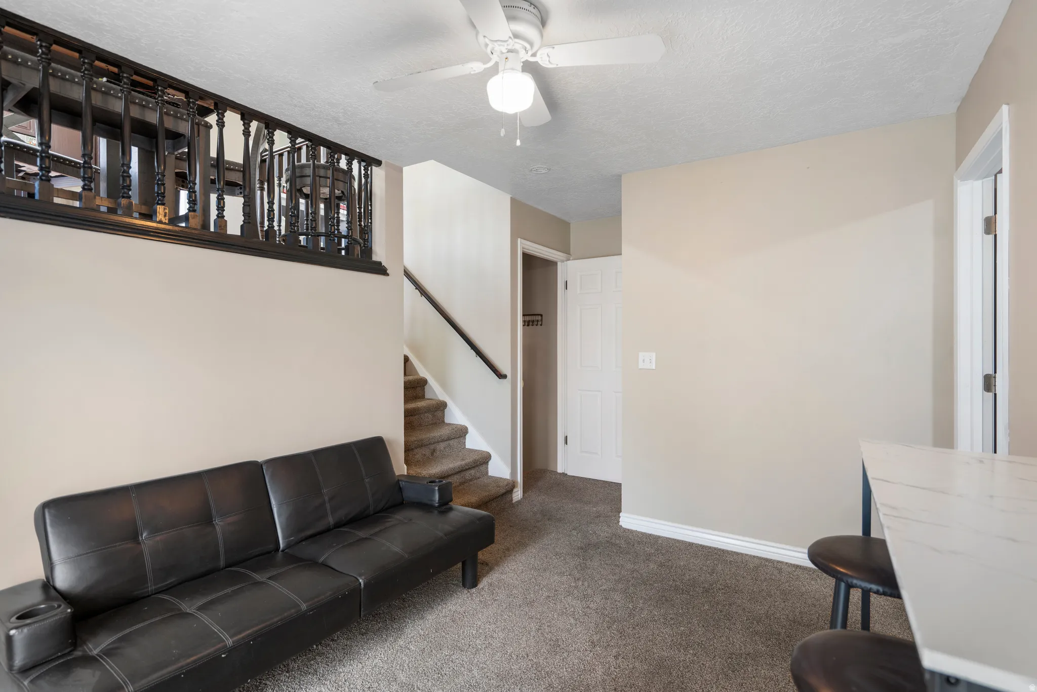 Carpeted living space featuring a ceiling fan, a staircase with a dark handrail, and a decorative dark wood railing on the upper level
