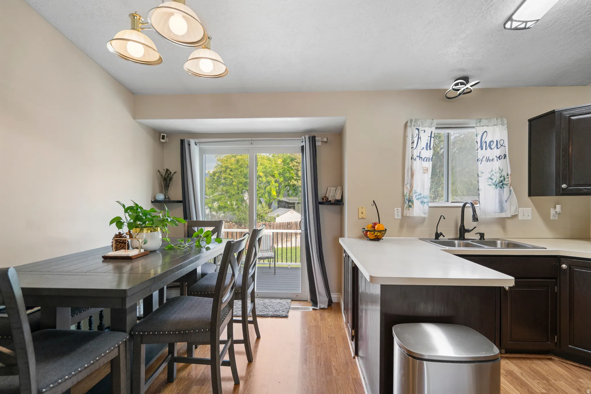 Wood-finish flooring, dark wood cabinetry, light countertops, kitchen sink with matte black faucet, and a sliding glass door to an outdoor deck