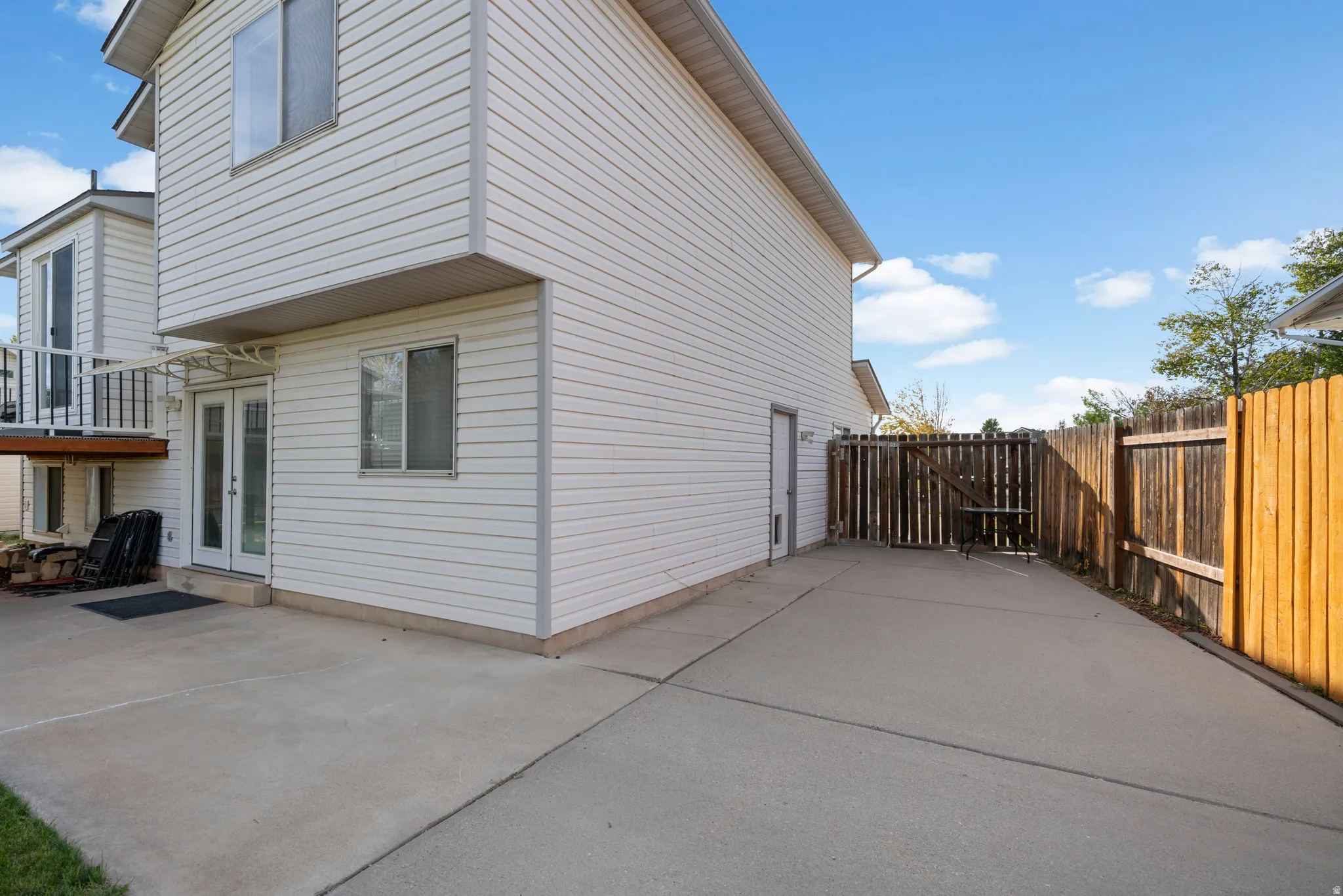 Rear exterior with white horizontal siding, concrete patio, double French doors, and a wood privacy fence