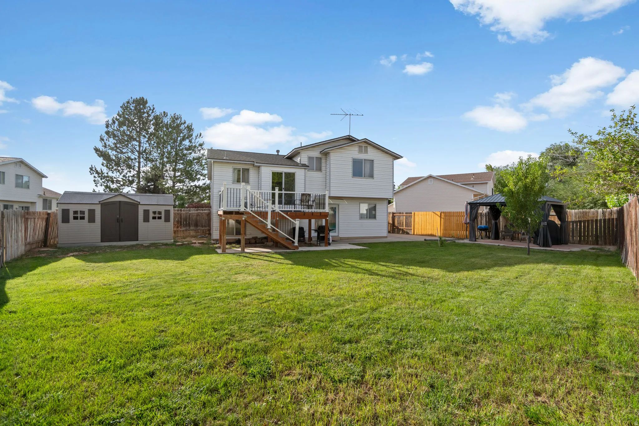 Expansive fenced backyard featuring a wood deck, storage shed, and mature trees