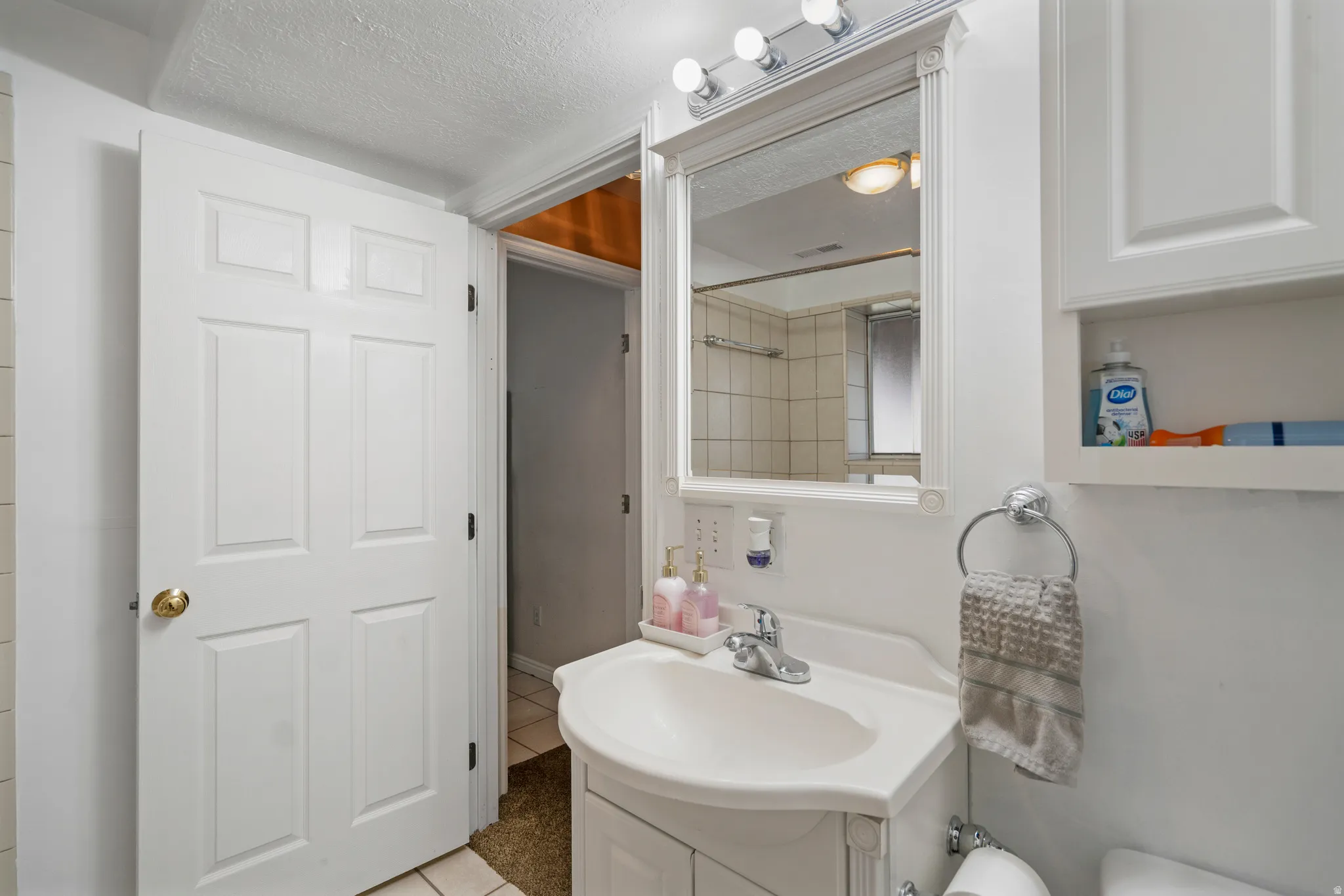 White paneled door, white vanity with integrated sink, wall-mounted mirror, and overhead strip lighting