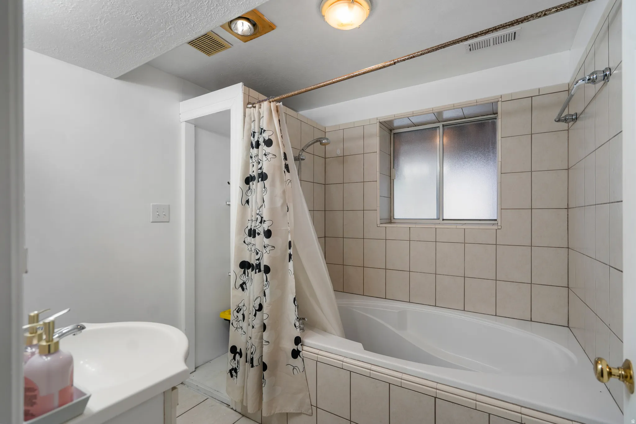 White ceramic tile shower surround with a built-in tub, textured glass window, and a wall-mounted light fixture