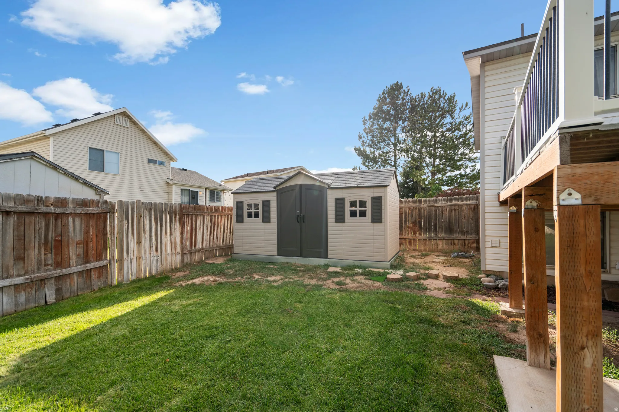 Fenced backyard featuring a manicured lawn, a detached storage shed, and an elevated wood deck