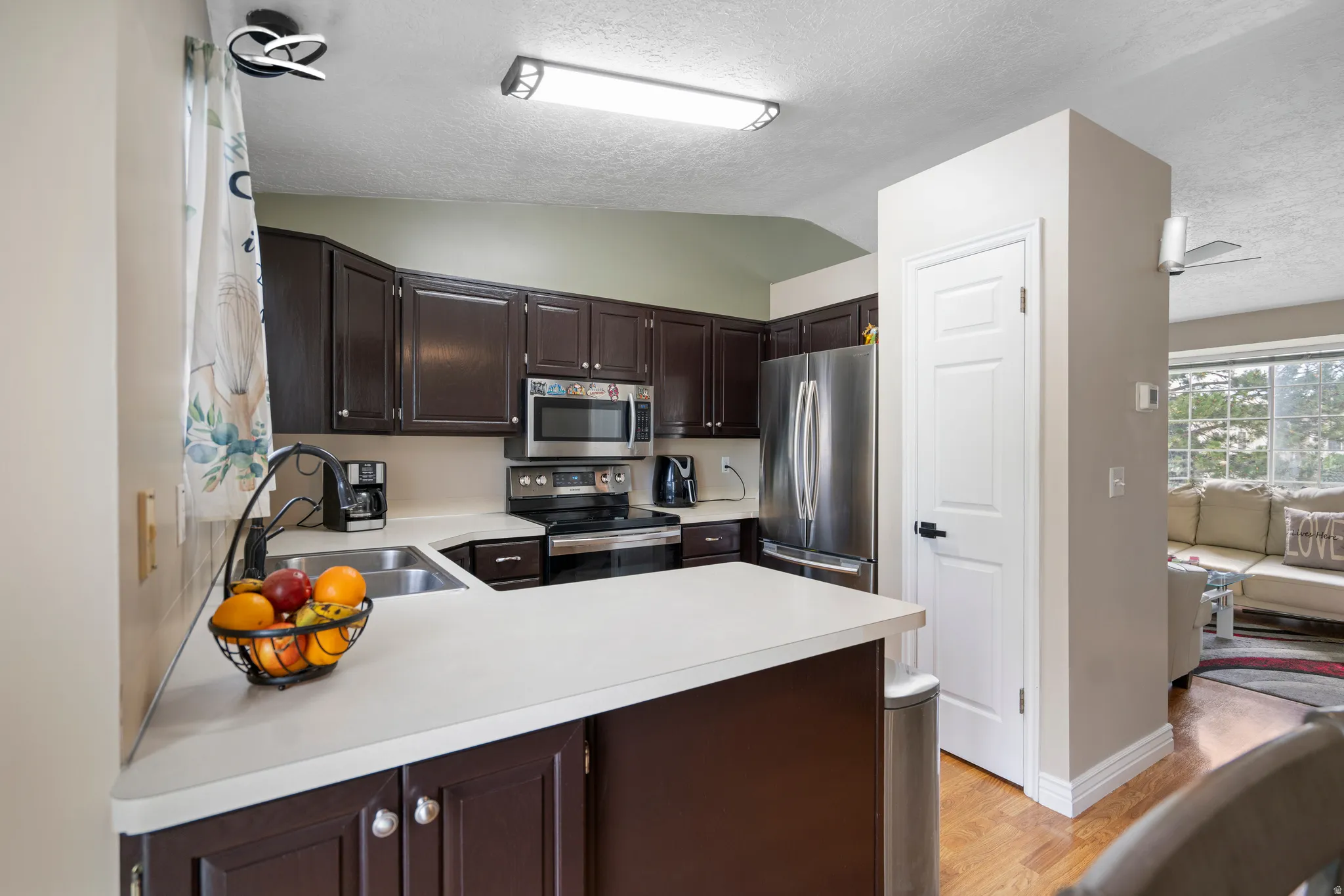 Kitchen featuring dark wood-finish cabinetry, stainless steel appliances, light-toned countertops, and wood-finish flooring