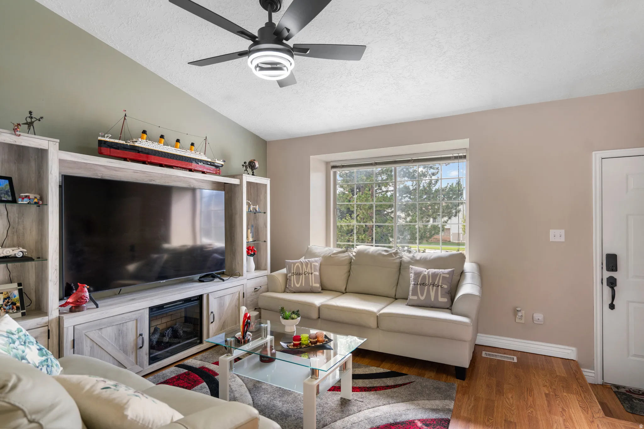 Vaulted ceiling with a ceiling fan, a large window, and wood-finish flooring