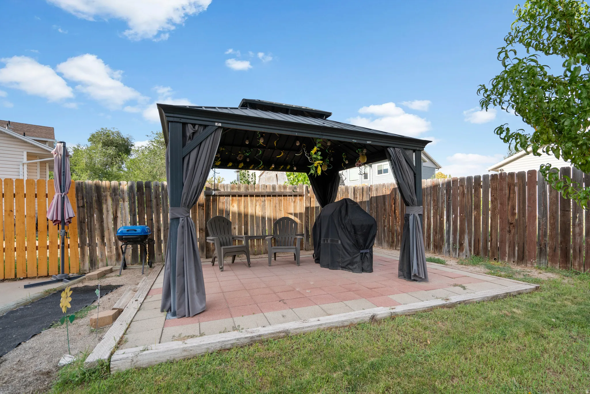 Paved patio featuring a gazebo with privacy curtains, wood fencing, and a grassy area