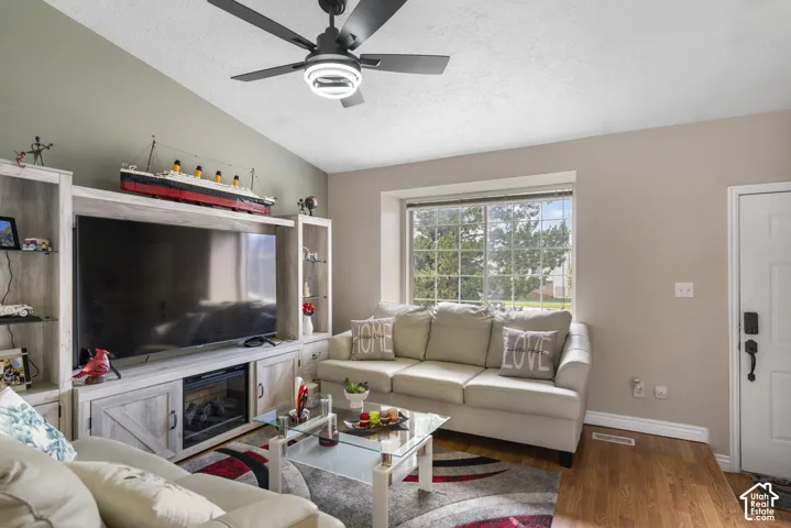 Vaulted ceiling with a ceiling fan, a large window, and wood-finish flooring