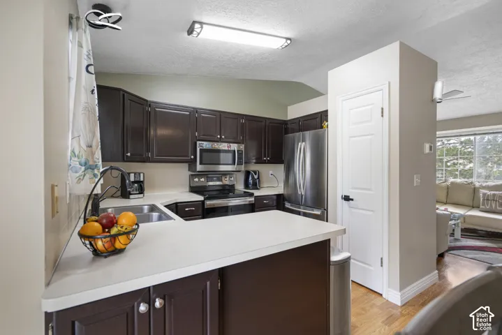 Kitchen featuring dark wood-finish cabinetry, stainless steel appliances, light-toned countertops, and wood-finish flooring