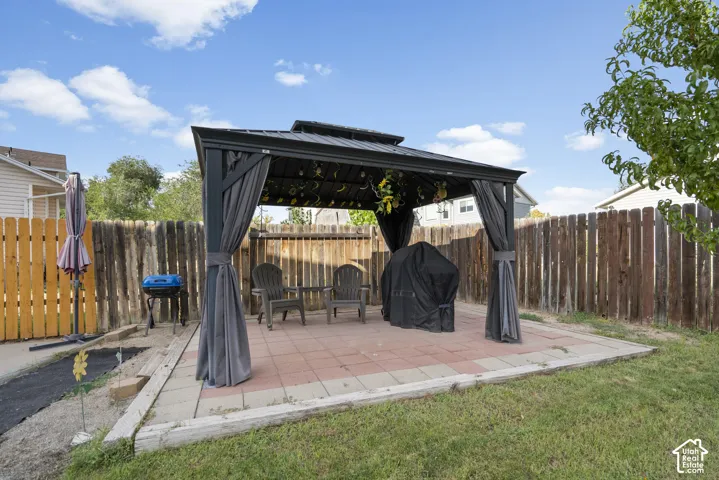 Paved patio featuring a gazebo with privacy curtains, wood fencing, and a grassy area