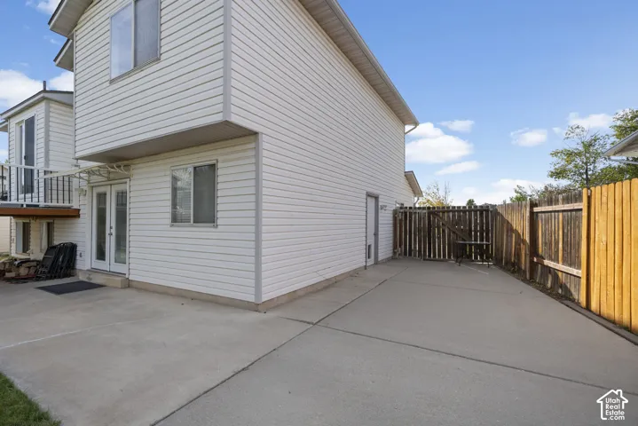 Rear exterior with white horizontal siding, concrete patio, double French doors, and a wood privacy fence