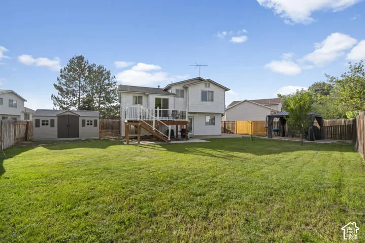 Expansive fenced backyard featuring a wood deck, storage shed, and mature trees