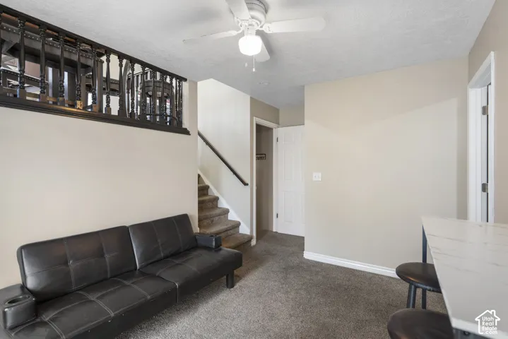 Carpeted living space featuring a ceiling fan, a staircase with a dark handrail, and a decorative dark wood railing on the upper level
