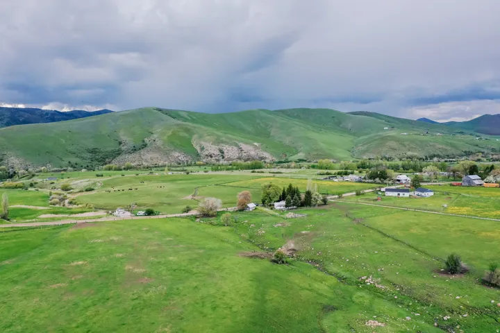 Expansive green fields with rolling hills, distant mountain backdrop, and scattered rural structures