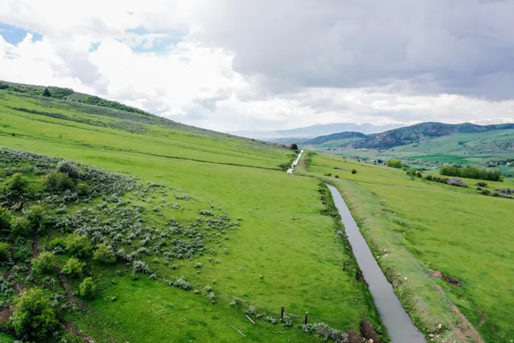 Expansive green terrain with a visible water channel, featuring distant mountains