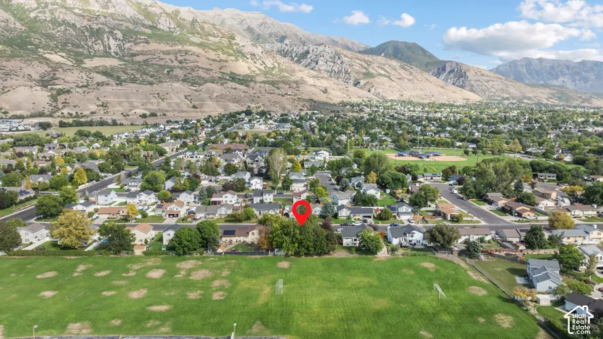 Residential neighborhood with a manicured green field, surrounded by established trees, and mountainous terrain in the background