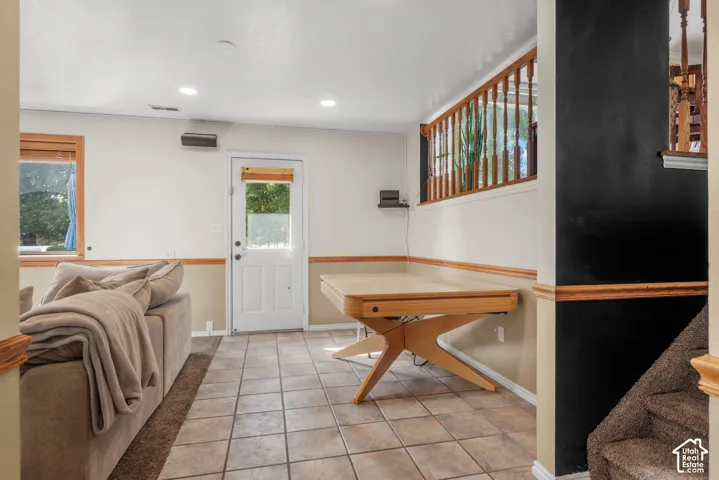 Recessed ceiling lighting, tile flooring, wood-finish trim, white paneled door with glass insert, and a wood spindle railing