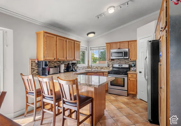 Kitchen featuring wood cabinetry, stainless steel appliances, a multi-tone tile backsplash, granite countertops, and tile flooring