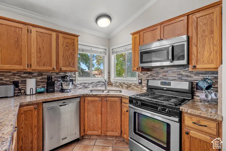 Kitchen featuring wood cabinetry, stainless steel appliances, speckled countertops, a tile backsplash, and a corner sink with a window