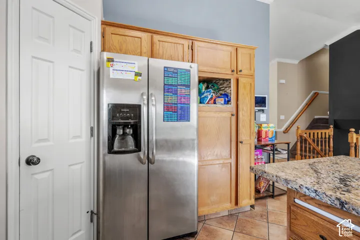 Stainless steel French door refrigerator, wood-finish cabinetry, tile flooring, and a stone countertop