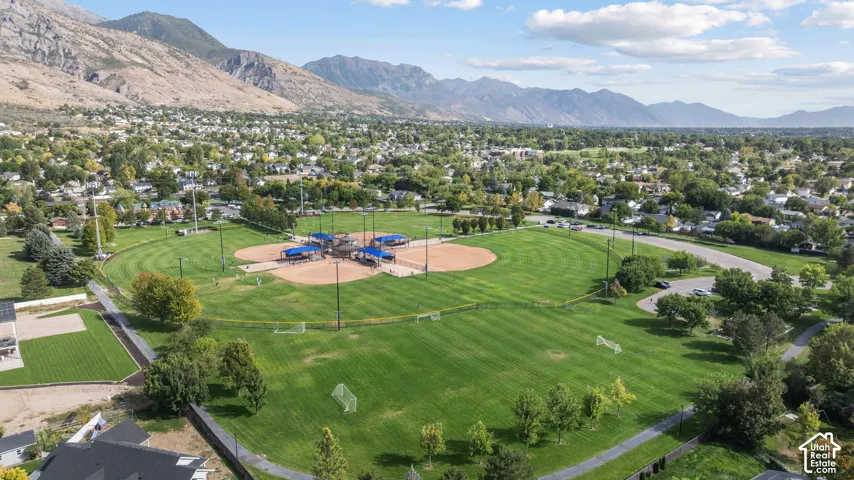 Expansive green space featuring multiple sports fields, a baseball diamond with covered dugouts, surrounding residential areas, and distant mountain ranges