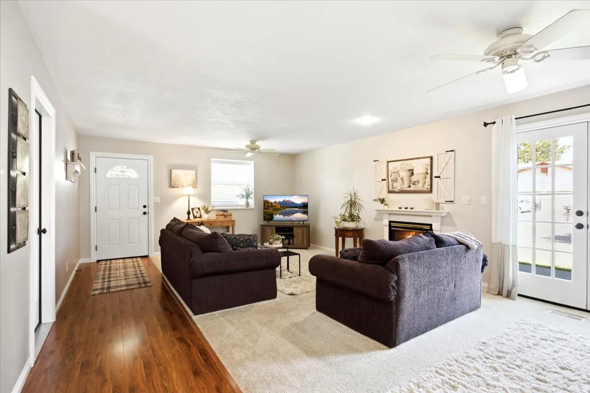 Living area featuring wood-finish flooring, a fireplace with a white mantel, and a ceiling fan