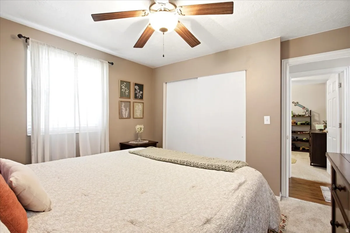 Ceiling fan with wood-finish blades, white sliding closet doors, and light-toned carpeting