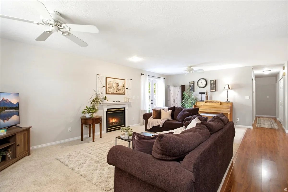Living area featuring a fireplace with a white mantel, ceiling fans, and a mix of carpet and wood-finish flooring