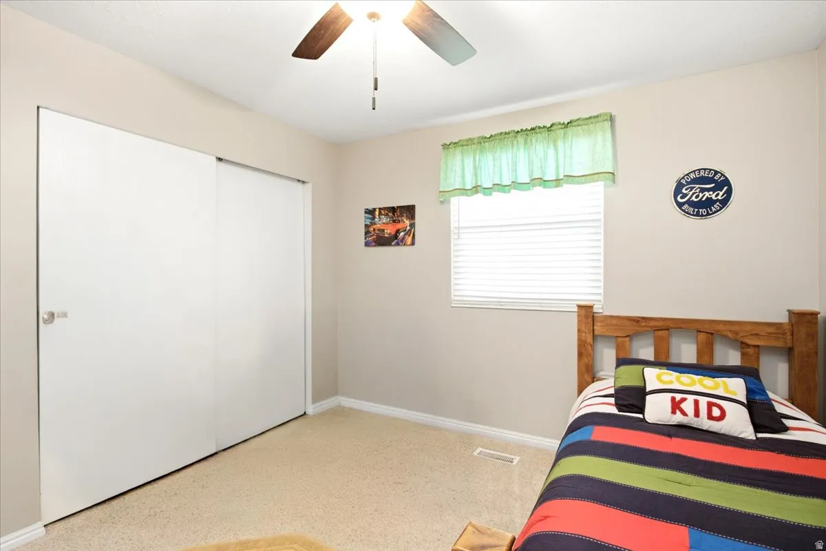 Sliding closet doors, ceiling fan with light fixture, window with blinds, and neutral wall paint