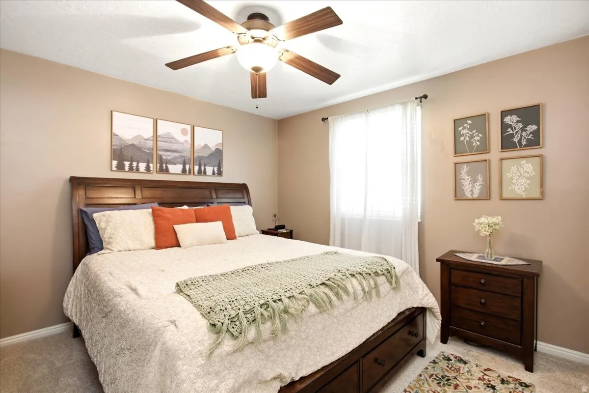 Recessed window with white blinds, ceiling fan with integrated lighting, wood-finish headboard, and carpeted flooring