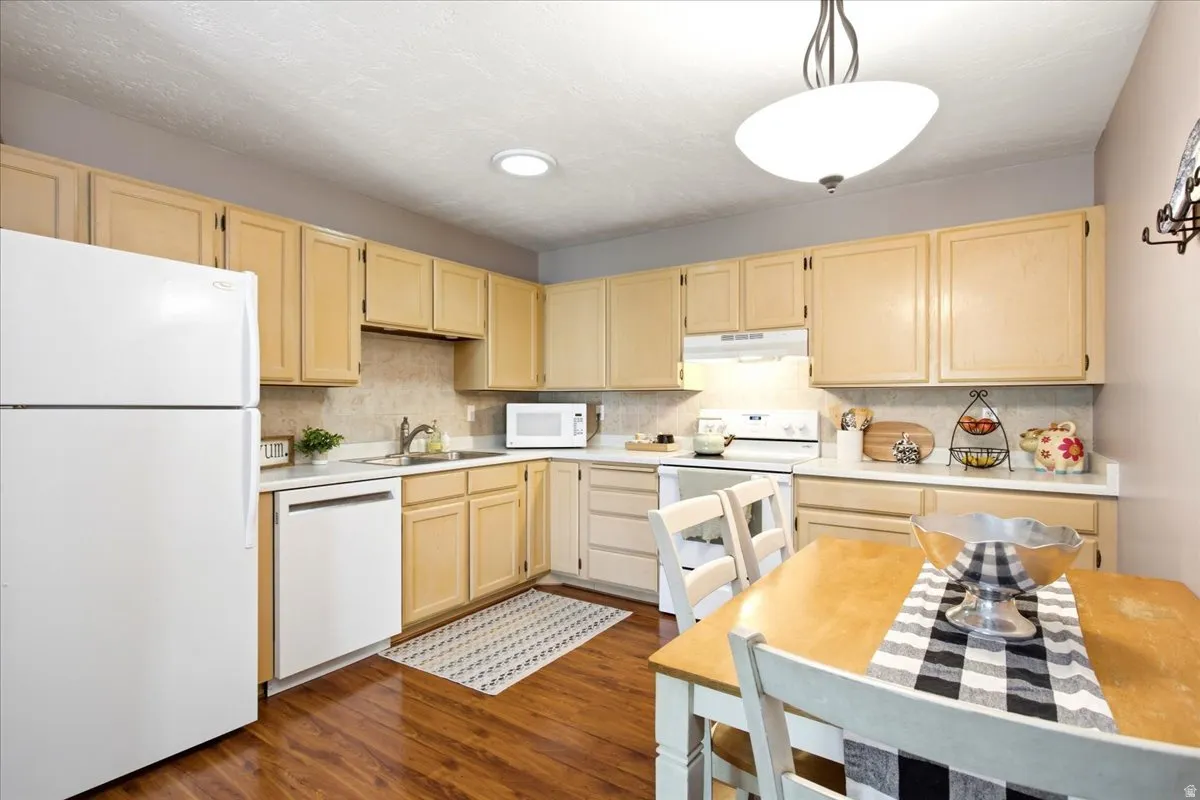 Wood-finish flooring with a white appliance package, light wood cabinetry, and recessed lighting