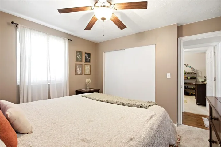 Ceiling fan with wood-finish blades, white sliding closet doors, and light-toned carpeting