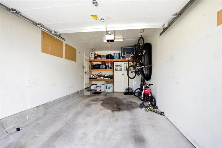 Concrete flooring, white painted walls, exposed garage door tracks, built-in shelving, and a wall-mounted storage rack