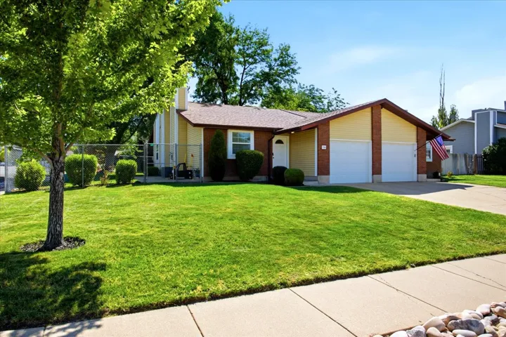 Yellow siding exterior with brick accents, attached two-car garage, and a concrete driveway