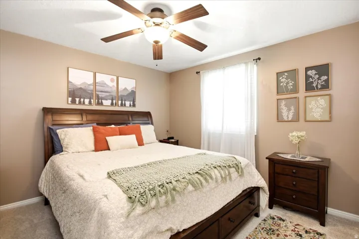 Recessed window with white blinds, ceiling fan with integrated lighting, wood-finish headboard, and carpeted flooring
