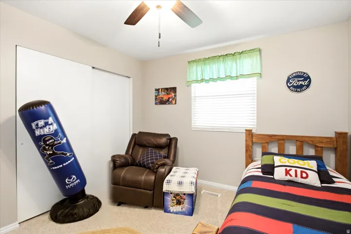 Recessed window with blinds, ceiling fan with light fixture, light-colored wall-to-wall carpeting, and white sliding closet doors