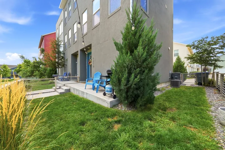 Stucco exterior featuring multiple windows, a concrete patio, and a grass lawn with mature plantings