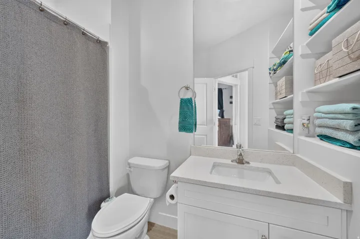 Bathroom featuring a single vanity with an undermount sink, quartz countertop, white cabinetry, and built-in shelving