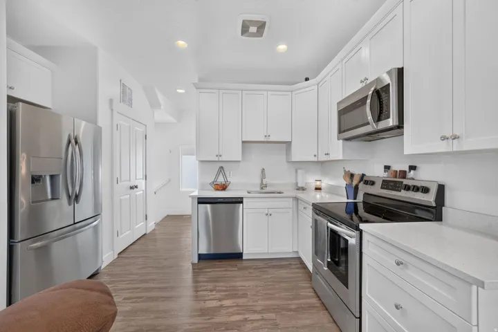 Kitchen featuring white cabinetry, stainless steel appliances, quartz countertops, wood-finish flooring, and recessed lighting