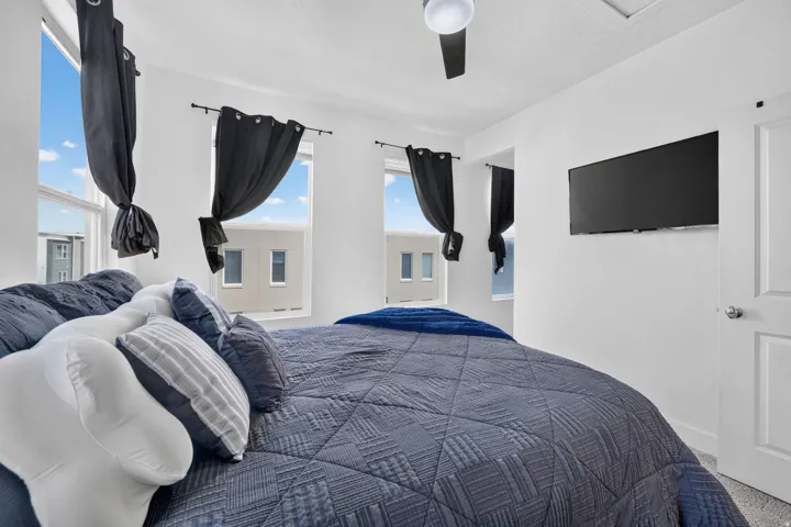 Primary bedroom with multiple windows, a ceiling fan, and wall-mounted television