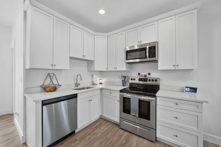 White shaker cabinetry, quartz countertops, stainless steel appliances, wood-finish flooring, and recessed lighting