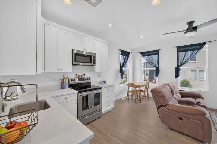 White shaker cabinetry with stainless steel appliances, quartz countertops, wood-finish flooring, recessed lighting, and a ceiling fan