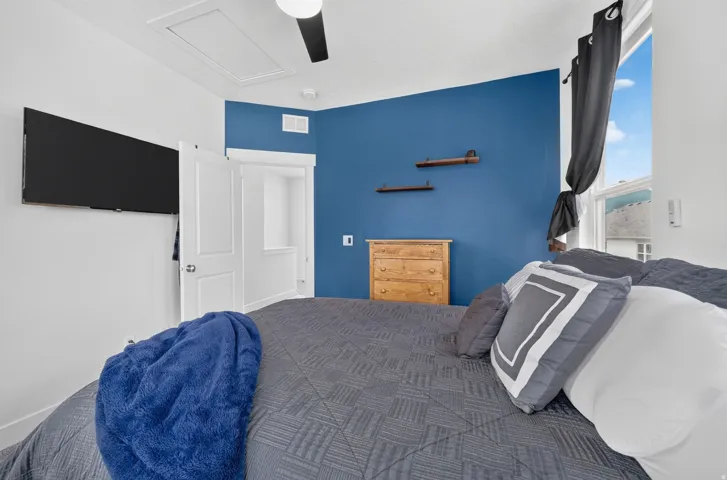 Primary bedroom with wall-mounted television, ceiling fan, accent wall, built-in shelving, and a many windows
