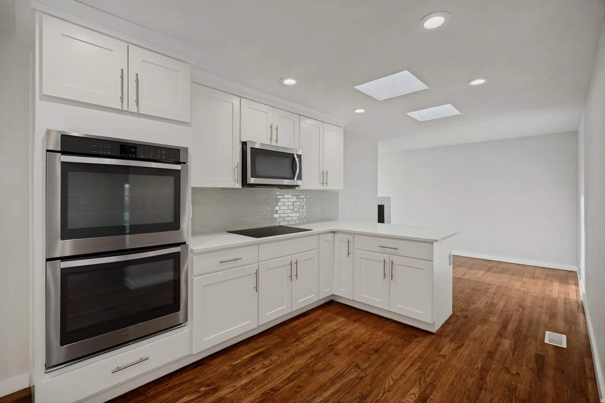 Kitchen featuring white shaker cabinetry, stainless steel double wall ovens, built-in microwave, white countertops, and wood-finish flooring