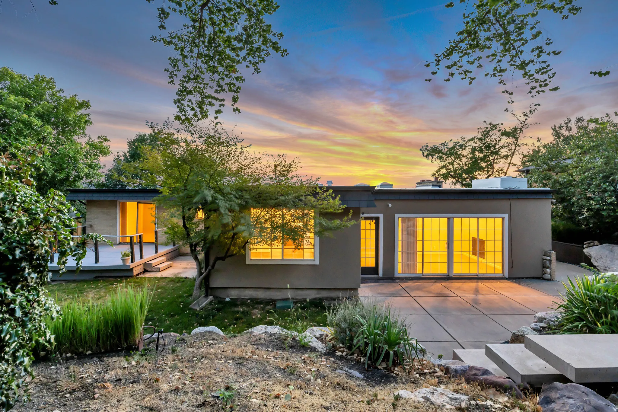 Modern exterior with a flat roofline, multiple sliding glass doors, a raised deck, and a concrete patio