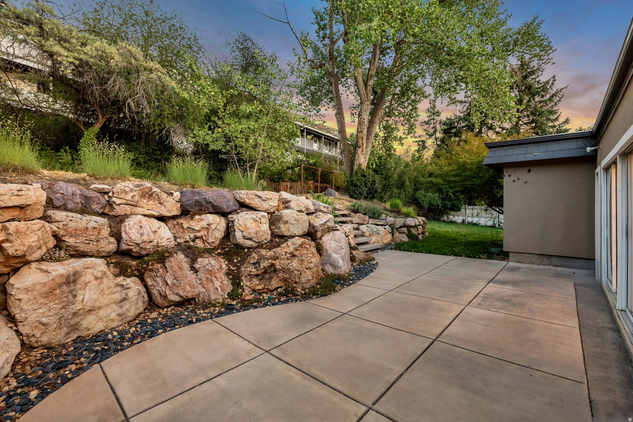 Paved patio area, stone retaining wall, mature trees, and landscaping