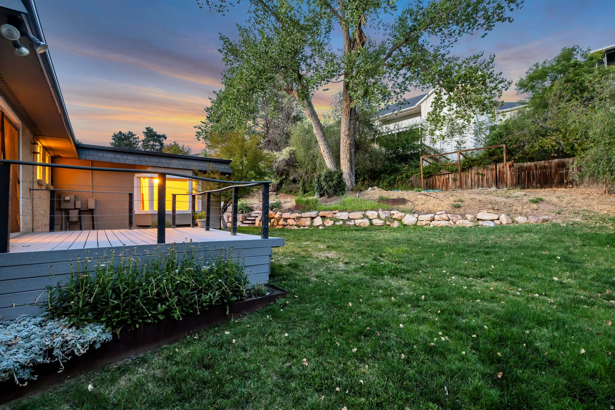 Expansive backyard featuring a manicured lawn, stone retaining wall, and mature trees