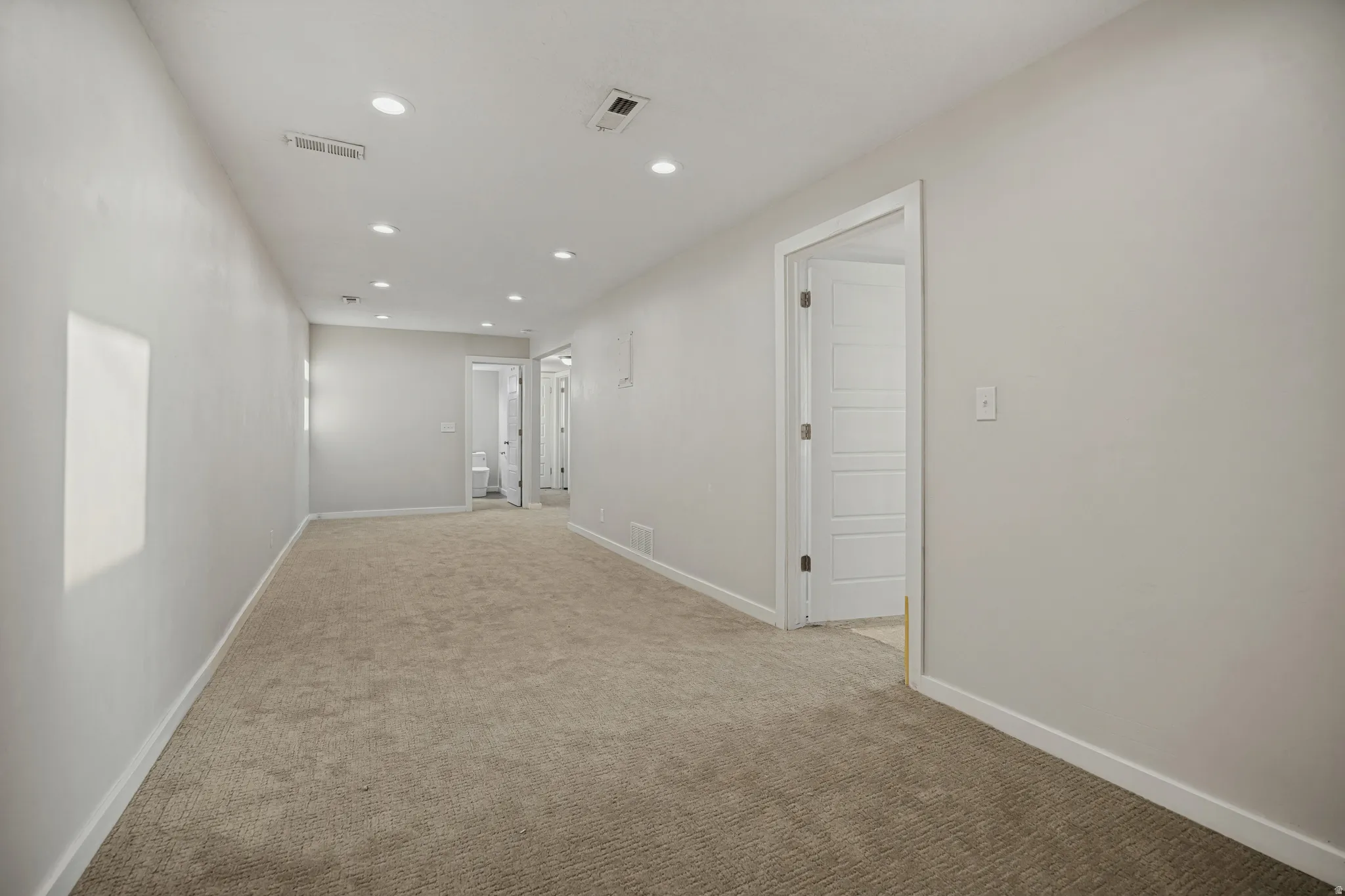 Recessed lighting, carpeted flooring, and a neutral wall color complement white trim and doors