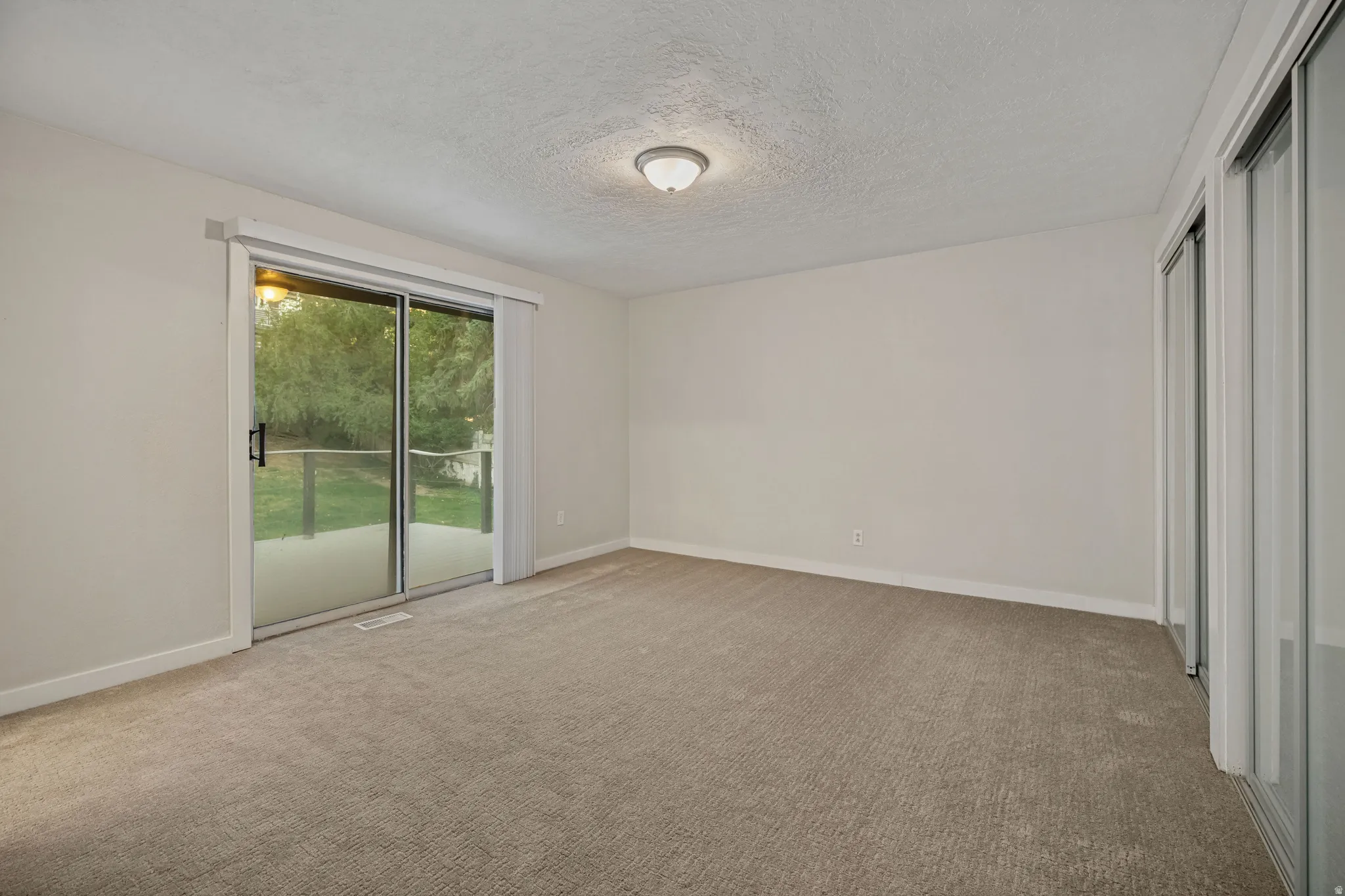 Sliding glass door leading to an outdoor patio, neutral carpeting, and a built-in closet with mirrored doors